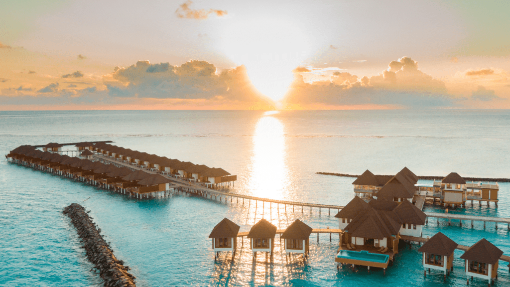 an aerial view of an overwater bungalow at sunset in the maldives